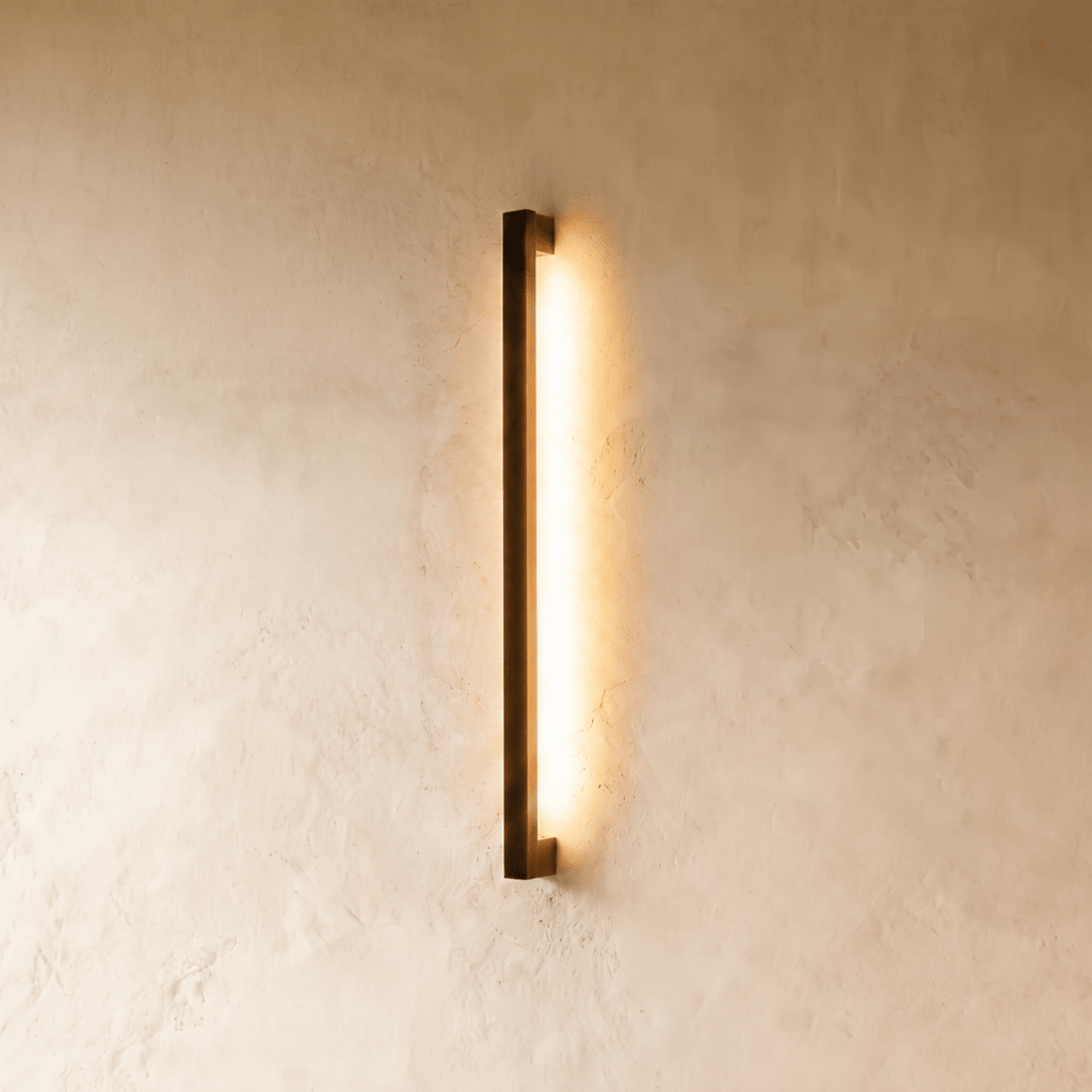 The black column wall light glows warm against plaster in this closer Clérachic hero shot, its slim vertical profile catching soft shadow.