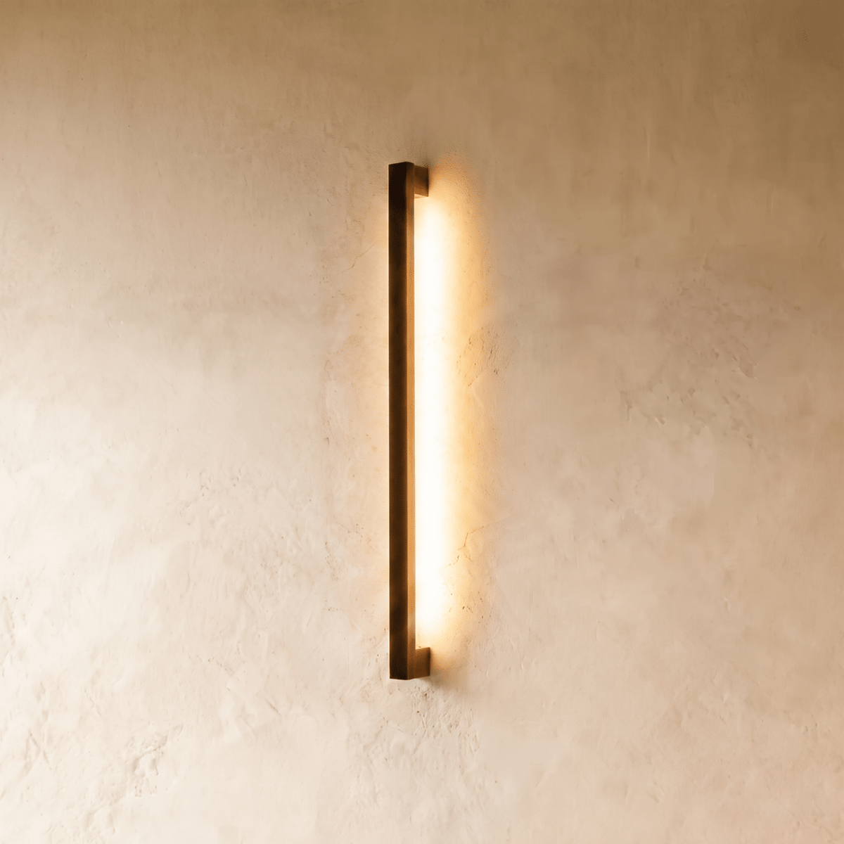 The black column wall light glows warm against plaster in this closer Clérachic hero shot, its slim vertical profile catching soft shadow.