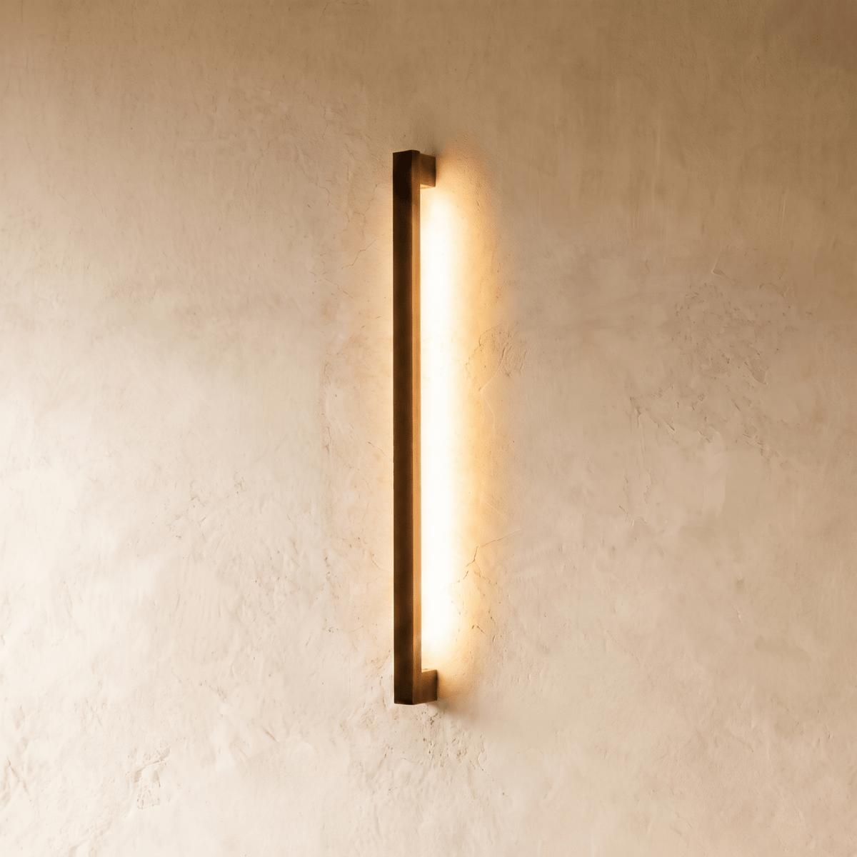 A further lit hero shot of the slim black column wall light shows its even warm wash down a textured plaster wall, styled by Clérachic.