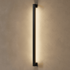 The matte black column wall light is shown fully lit here, its warm strip glowing the length of the fixture in this Clérachic hero shot.
