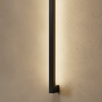 A close-up on the black column wall light's lower mounting bracket and square profile, glowing warm against plaster, Clérachic detail shot.