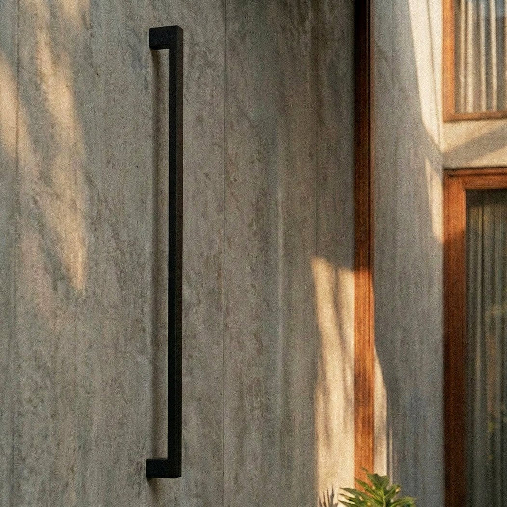 A closer crop shows the black column wall light mounted on ribbed concrete beside a large monstera leaf, Clérachic detail shot.