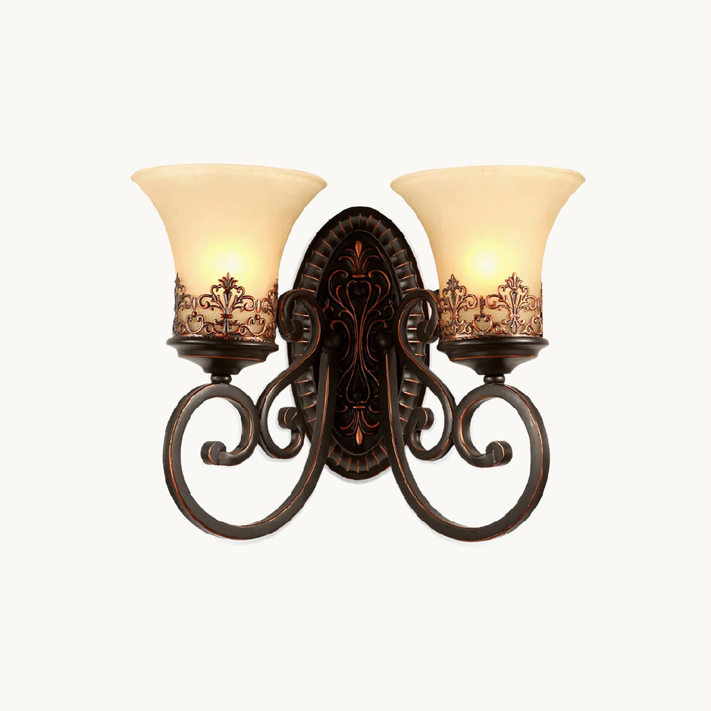 A two-arm Clérachic wall lamp with scrolled dark bronze arms and cream glass bell shades, lit on a white backdrop.