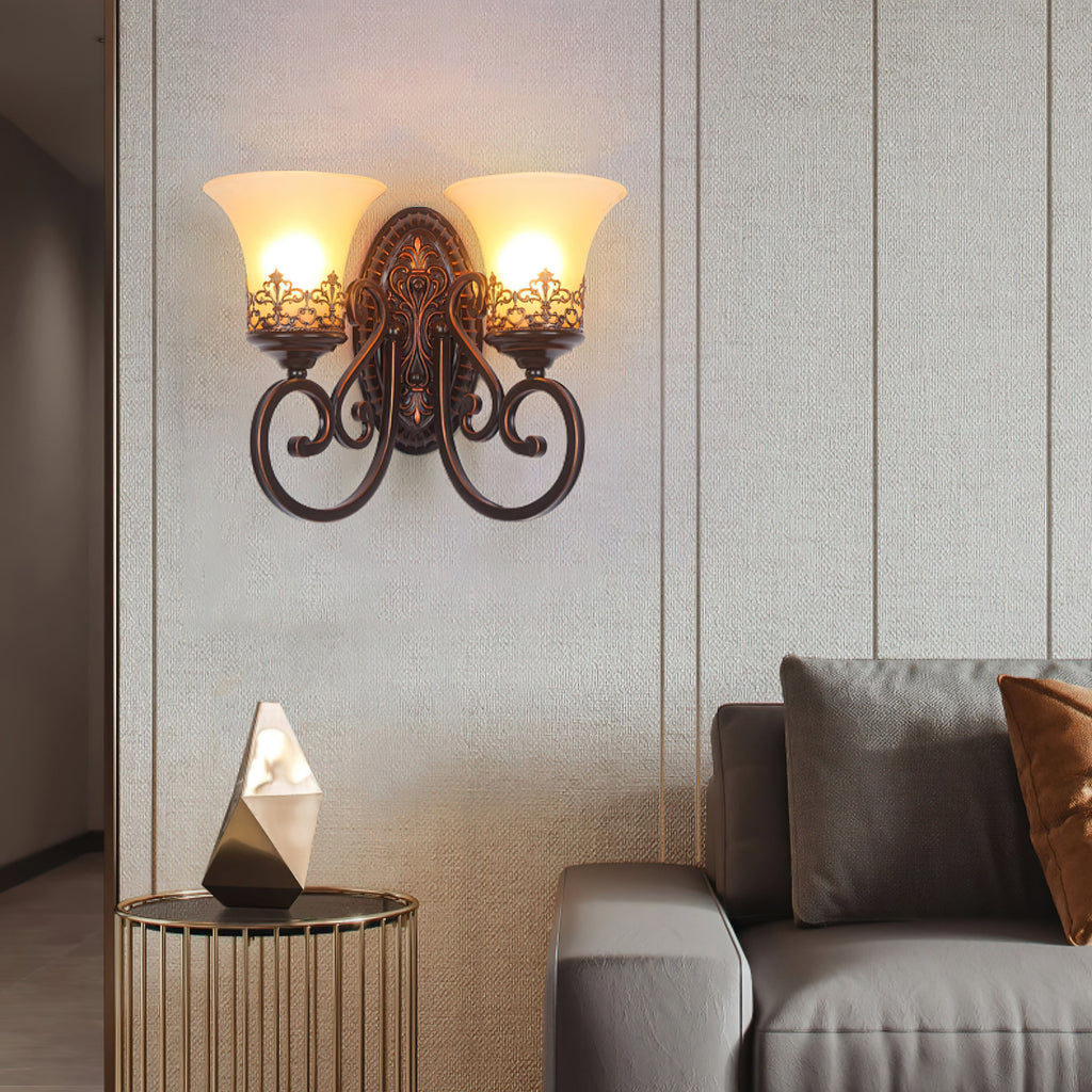 A two-arm Clérachic wall lamp glows above a grey sofa and a gold cage side table holding a faceted ornament.