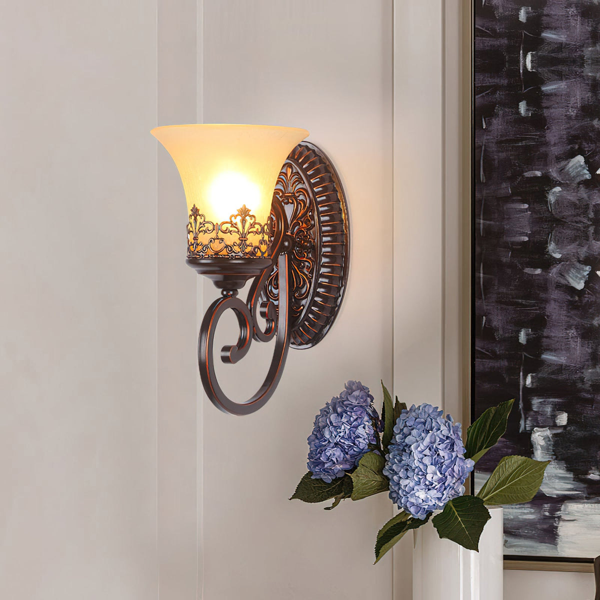 A single-arm Clérachic wall lamp lights a pale wall next to a vase of blue hydrangeas and a dark abstract canvas.