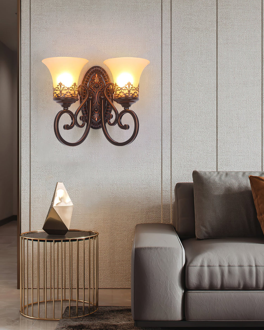 Two glowing glass shades on scrolled arms, this Clérachic wall lamp sits above a gold side table and a grey sofa.