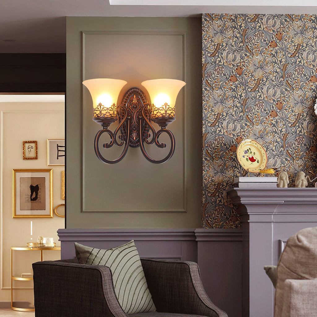 A two-arm Clérachic wall lamp glows against a sage panel, with a gilt plate on the mantel and an armchair below.