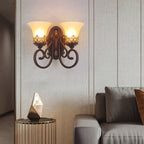 A two-arm Clérachic wall lamp hangs on a striped, pale wall above a faceted ornament and a grey sofa.