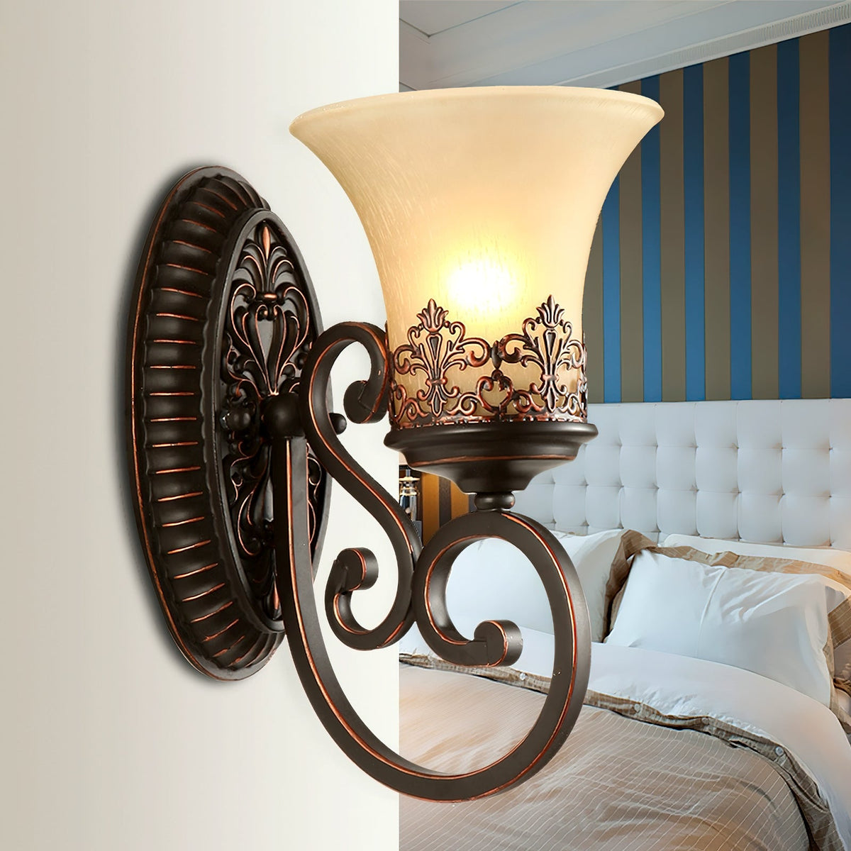 Close view of a single-arm Clérachic wall lamp, its glass bell shade lit above a tufted white headboard.