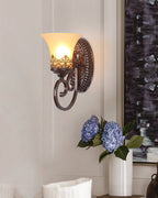 A single-arm Clérachic wall lamp on a pale wall, above a white vase of blue flowers and next to a dark canvas.
