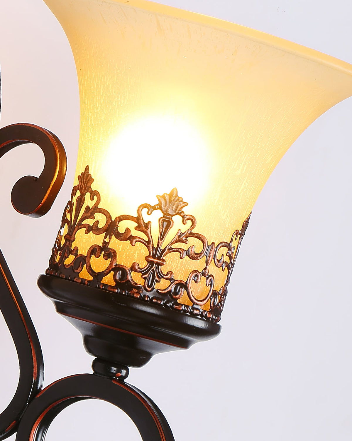 Close view of one lit glass shade on this Clérachic wall lamp, with the cut-metal filigree band at its base.