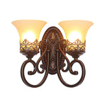 A lit two-arm Clérachic wall lamp with scrolled dark bronze arms, cut out against a plain white background.