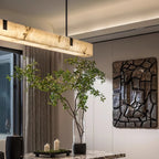 The Clérachic Black Linear Chandelier glows warm above a marble dining table beside a potted olive tree and dark wall art.