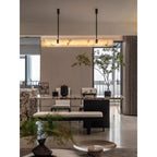 The Clérachic Black Linear Chandelier illuminates an open dining and kitchen space with plants and a marble island.
