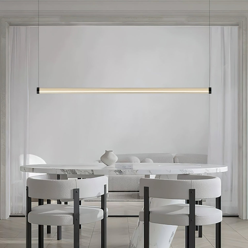 This Clérachic linear pendant hangs over a marble oval table with boucle chairs, its slim lit tube running across a pale panelled wall.