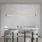 This Clérachic linear pendant hangs over a marble oval table with boucle chairs, its slim lit tube running across a pale panelled wall.