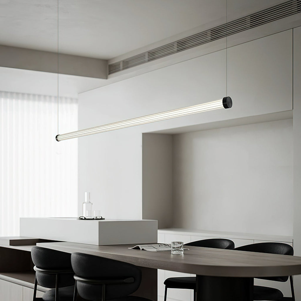 Angled view of a Clérachic linear pendant above a long dark oval table, its tube tilted in a grey kitchen with a high ceiling vent.