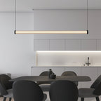 Over a dark rectangular table with black shell chairs, this Clérachic linear pendant hangs level in front of a kitchen with a lit backsplash.