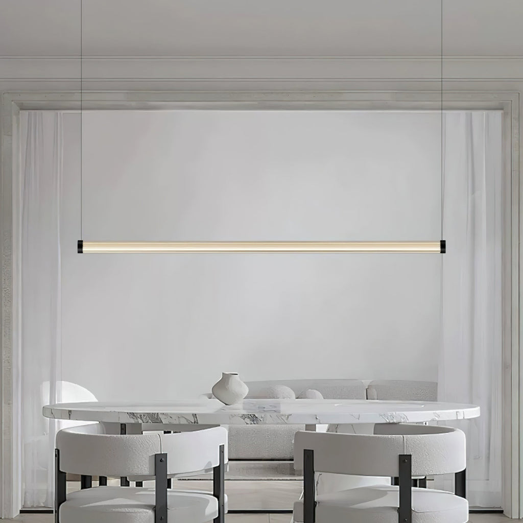 A Clérachic linear pendant lit above a marble table with white boucle chairs and a small vase, its tube centred on a pale wall.