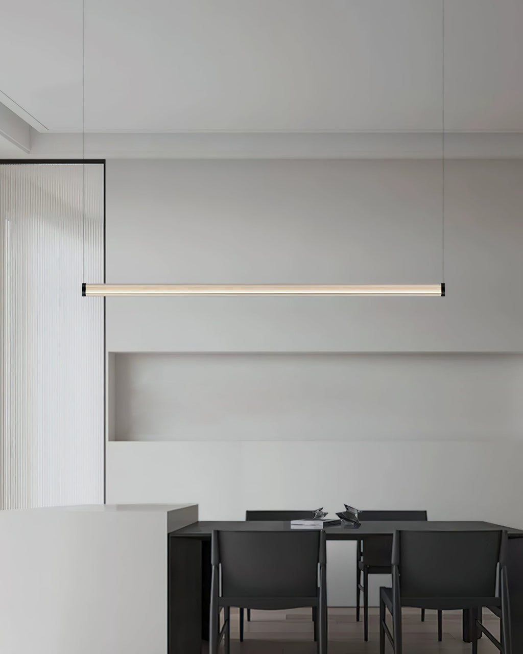 Seen from further back, this Clérachic linear pendant hangs above a dark dining table with black chairs in a pale grey room.