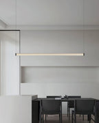 Seen from further back, this Clérachic linear pendant hangs above a dark dining table with black chairs in a pale grey room.
