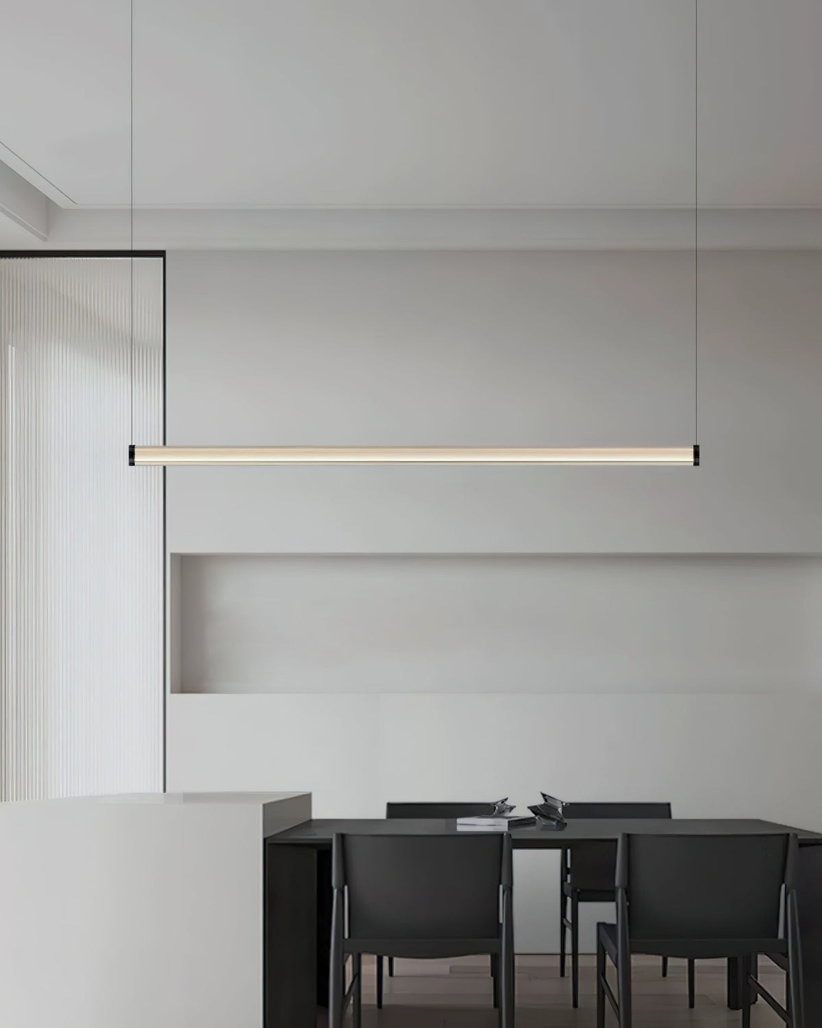 Seen from further back, this Clérachic linear pendant hangs above a dark dining table with black chairs in a pale grey room.