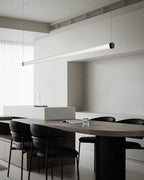 Tilted view of a Clérachic linear pendant above a dark oval table, with a glass carafe on a pale island behind it.