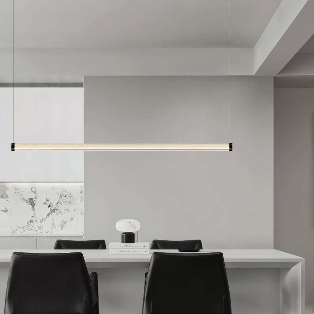 This Clérachic linear pendant hangs above a long white table with black chairs, with a marble-effect panel on the wall behind.