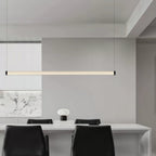 This Clérachic linear pendant hangs above a long white table with black chairs, with a marble-effect panel on the wall behind.
