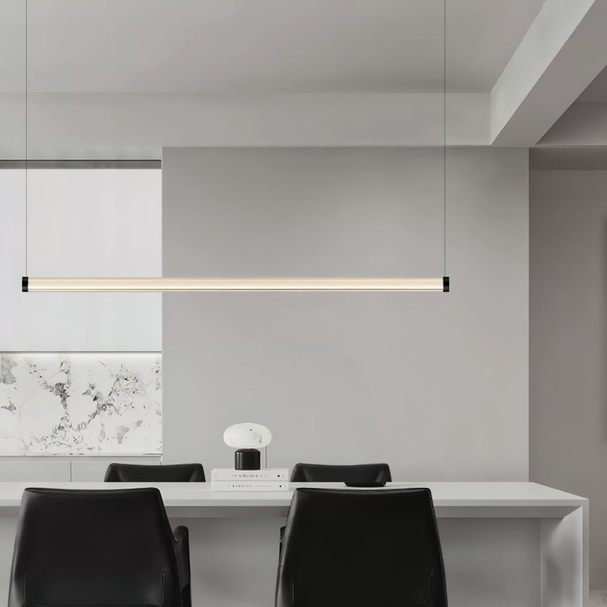 This Clérachic linear pendant hangs above a long white table with black chairs, with a marble-effect panel on the wall behind.