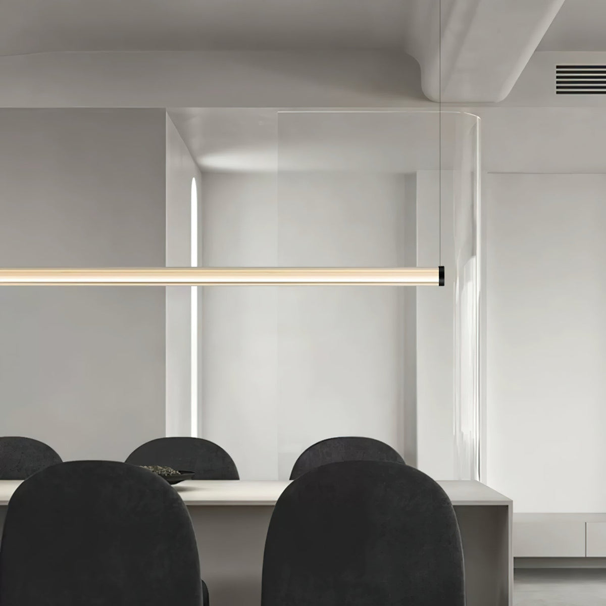 Close crop of a Clérachic linear pendant running across the frame, above black rounded dining chairs in a pale open-plan room.