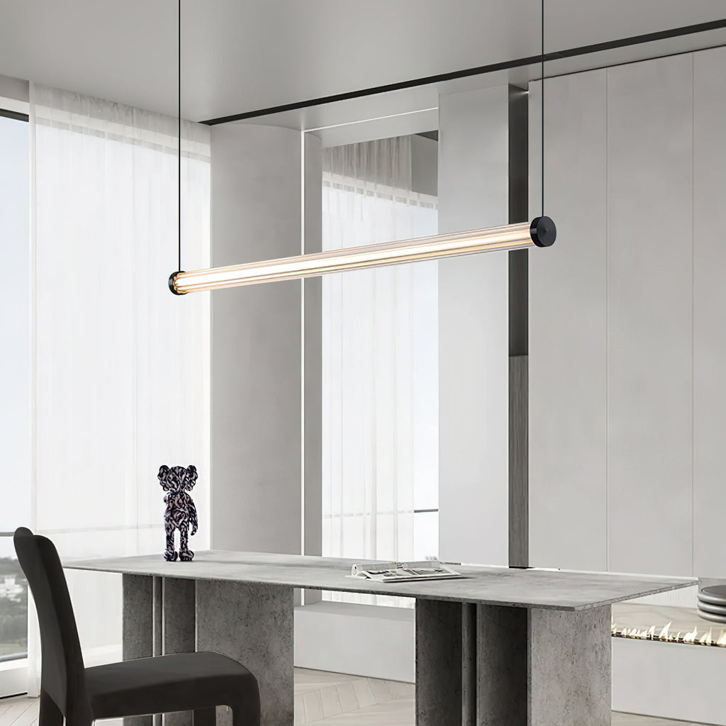 A Clérachic linear pendant angled above a stone-look console table with a small figurine, beside tall sheer-curtained windows.