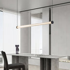 A Clérachic linear pendant angled above a stone-look console table with a small figurine, beside tall sheer-curtained windows.