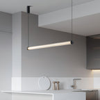 This Clérachic linear pendant hangs at a slant in a white kitchen, with a marble counter, a tap and wooden pepper mills below.