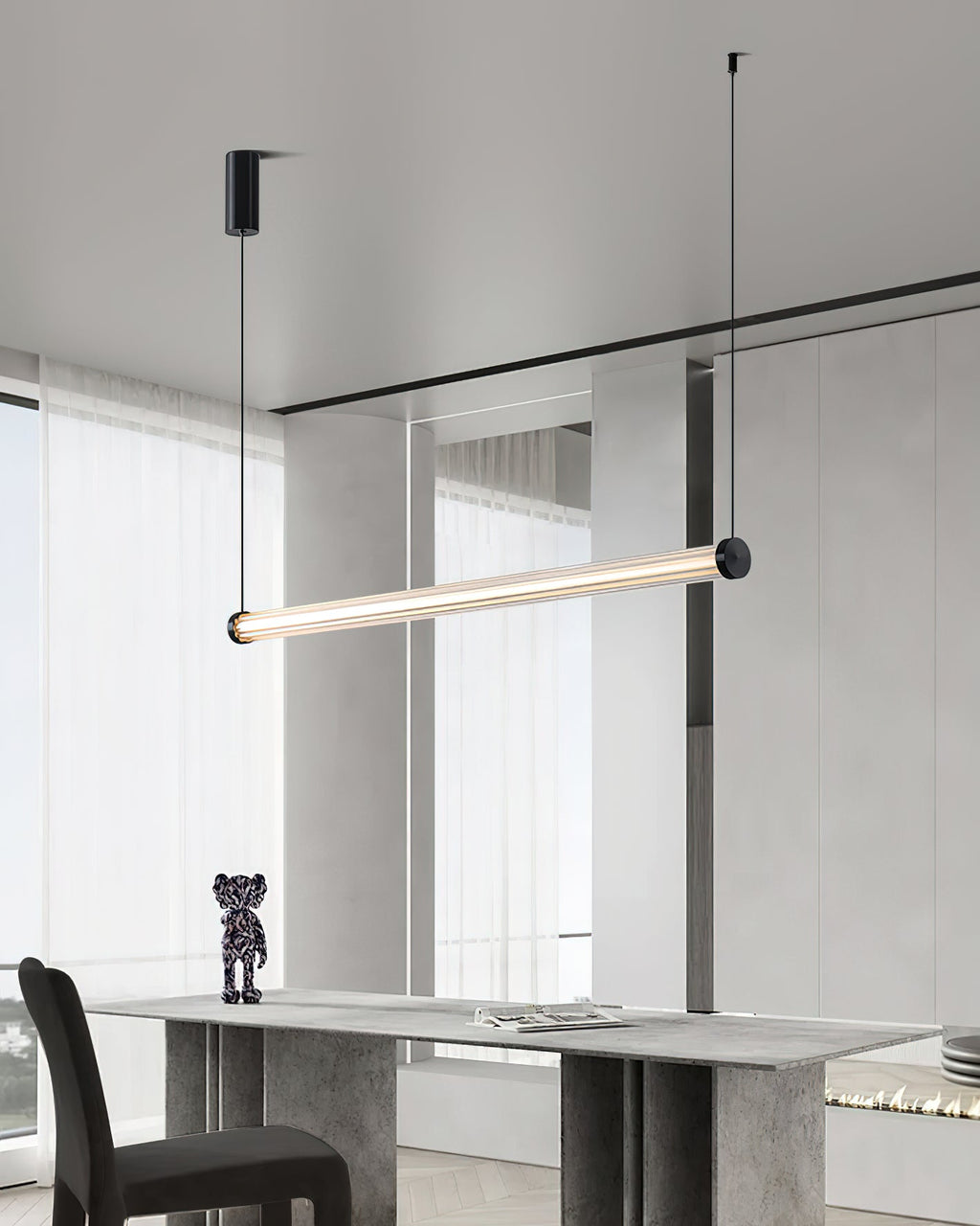 In a room with floor-length sheer curtains, this Clérachic linear pendant hangs at an angle above a grey stone table.
