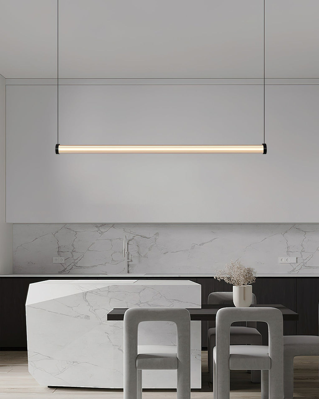 Hanging in front of a marble splashback and a stone island with grey chairs, this Clérachic linear pendant glows a soft warm white.