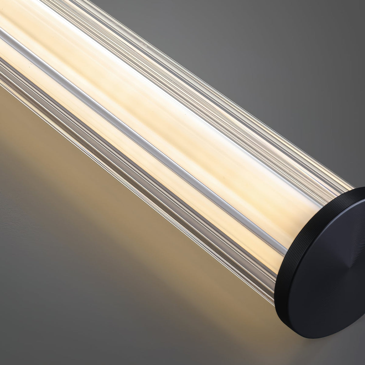 Close view of the ribbed glass tube on this Clérachic linear pendant, glowing warm beside a round black end cap.