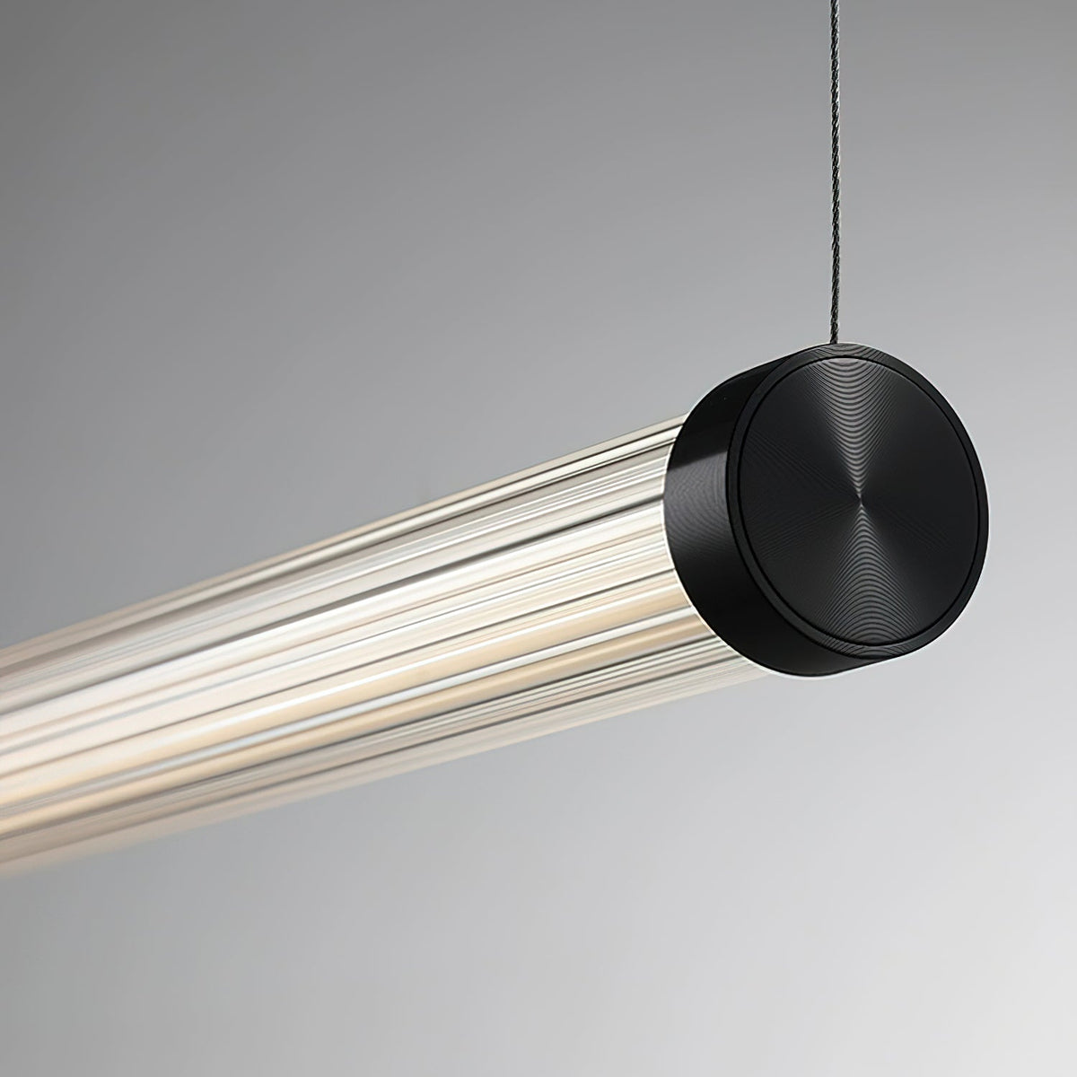 A Clérachic linear pendant on a pale grey backdrop, its black end cap with a ringed finish hung from a thin dark cable.