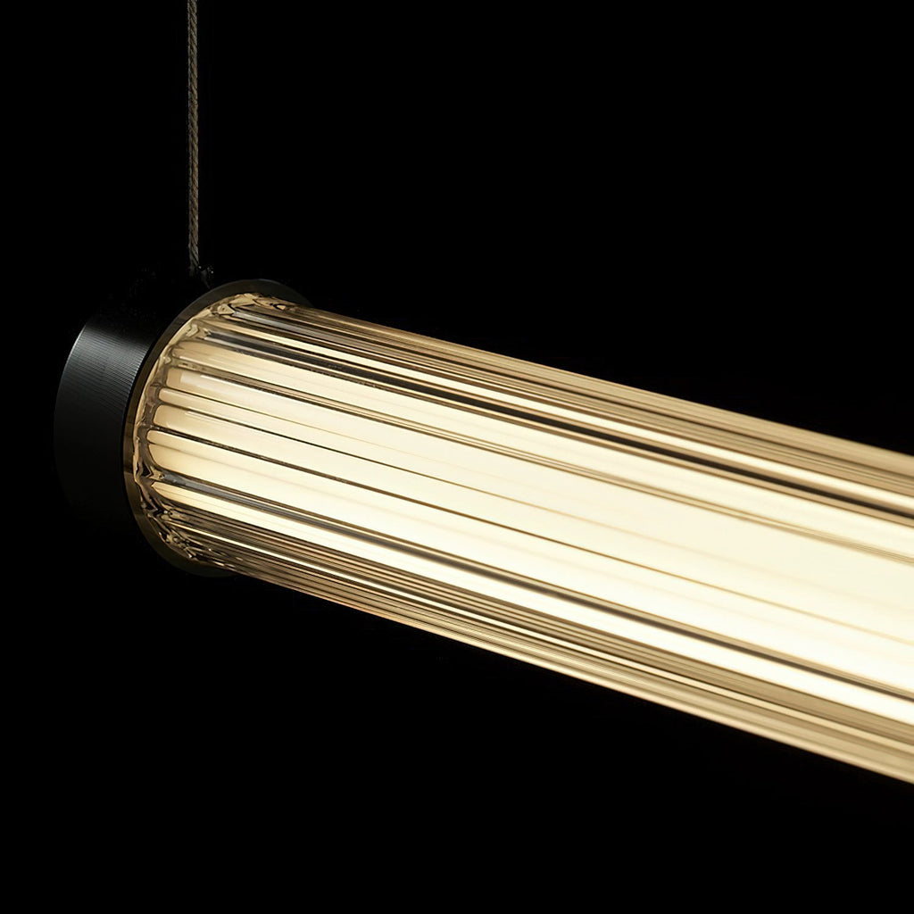 Lit against a black background, the ribbed clear tube of this Clérachic linear pendant glows warm beside its black end cap.