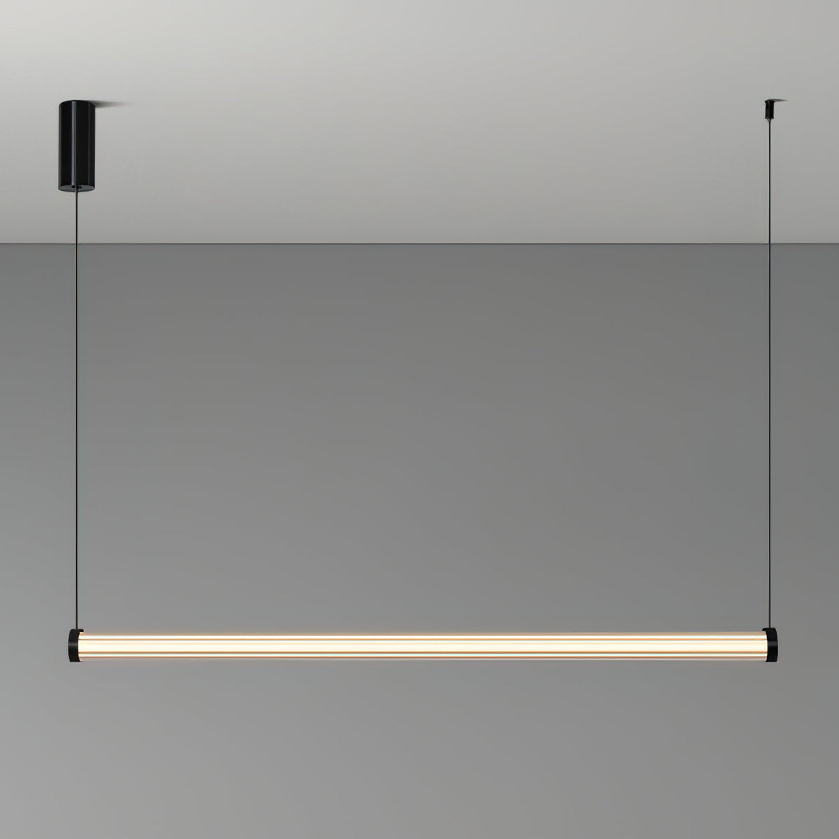 A Clérachic linear pendant lit on a grey backdrop, hung level from two thin cables, with a black cylinder canopy on the left.