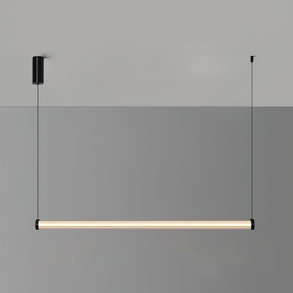 A level Clérachic linear pendant lit warm against a two-tone grey wall, with its black canopy and cable at either end.
