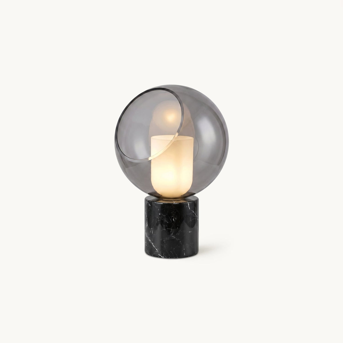 This Clérachic table lamp on a plain white backdrop, a smoke-grey glass sphere with a cut-away opening around a white glowing cylinder, on a black marble base.