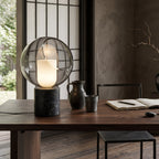Close view of this Clérachic table lamp on a dark wood desk, with a ceramic jug, a cup and an open notebook, by a paper-screen window.