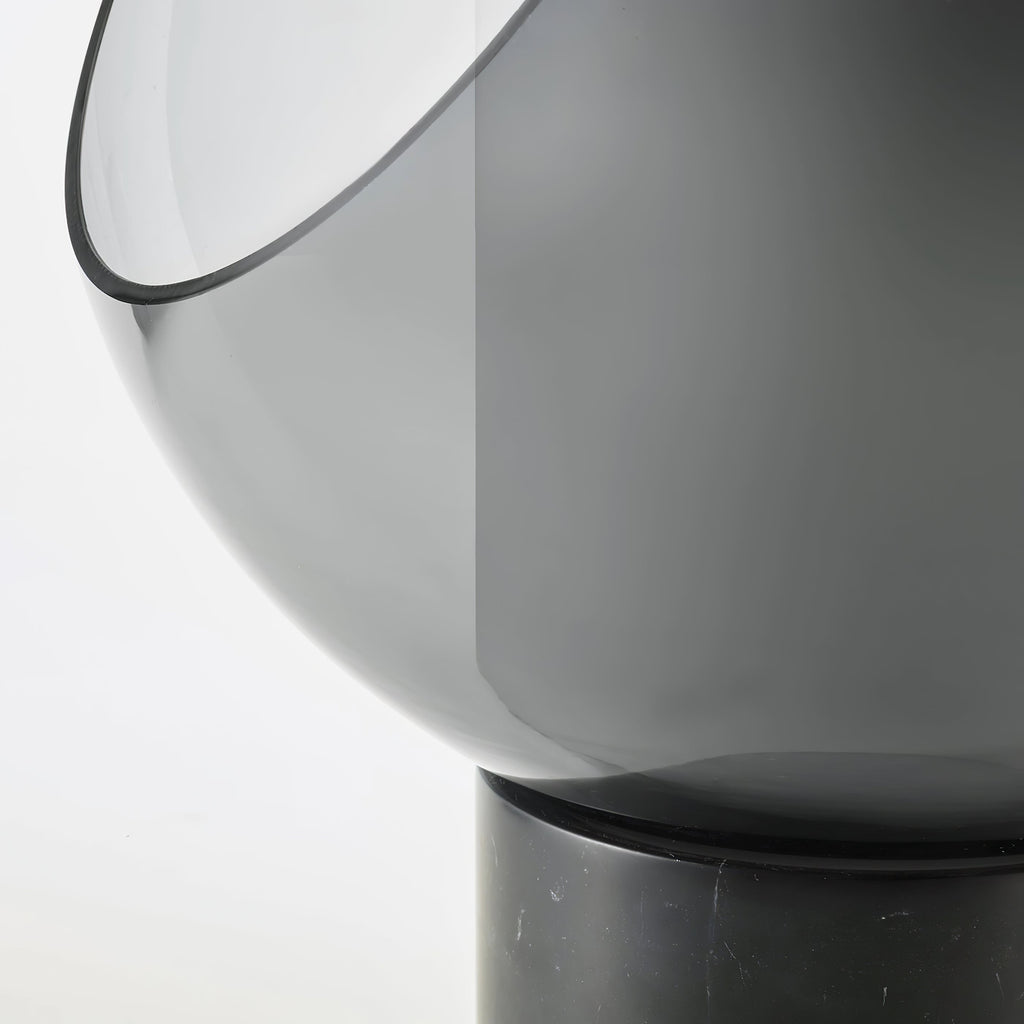Close view of the smoke-grey glass sphere's cut-away edge on this Clérachic table lamp, meeting its black marble base.