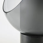Close view of the smoke-grey glass sphere's cut-away edge on this Clérachic table lamp, meeting its black marble base.