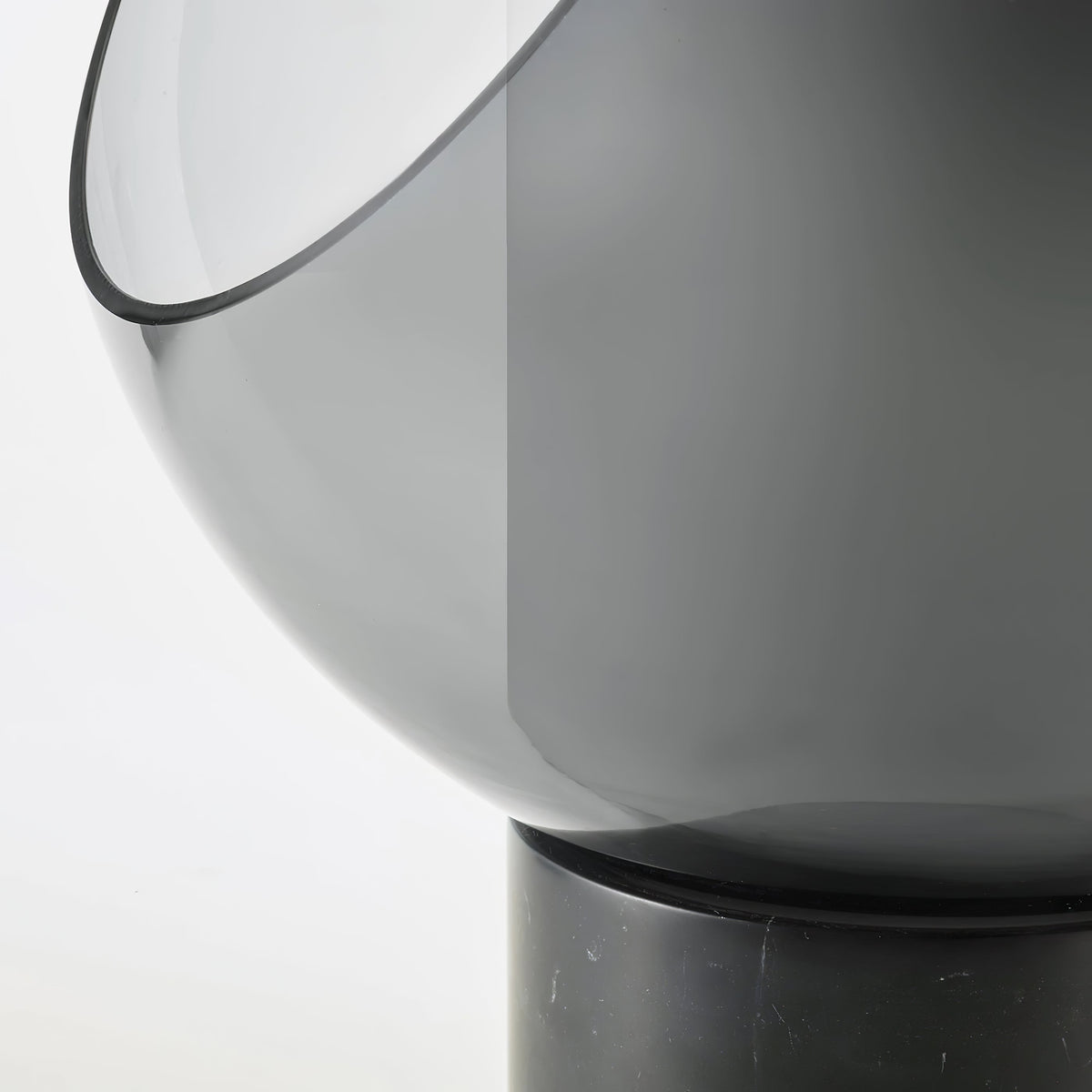 Close view of the smoke-grey glass sphere's cut-away edge on this Clérachic table lamp, meeting its black marble base.