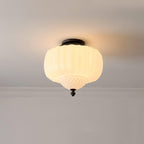 Lit ribbed white glass ceiling light from Clérachic with a black canopy, glowing warm below a cornice on a soft grey wall.
