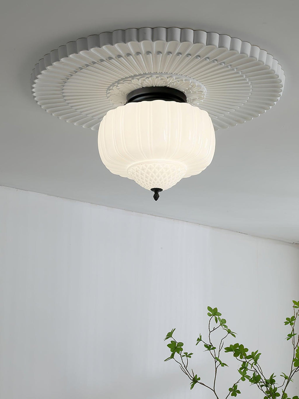 Clérachic ceiling light with a ribbed white glass shade and black canopy, set within a fluted plaster ceiling rose above a white wall.