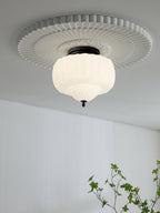 Clérachic ceiling light with a ribbed white glass shade and black canopy, set within a fluted plaster ceiling rose above a white wall.