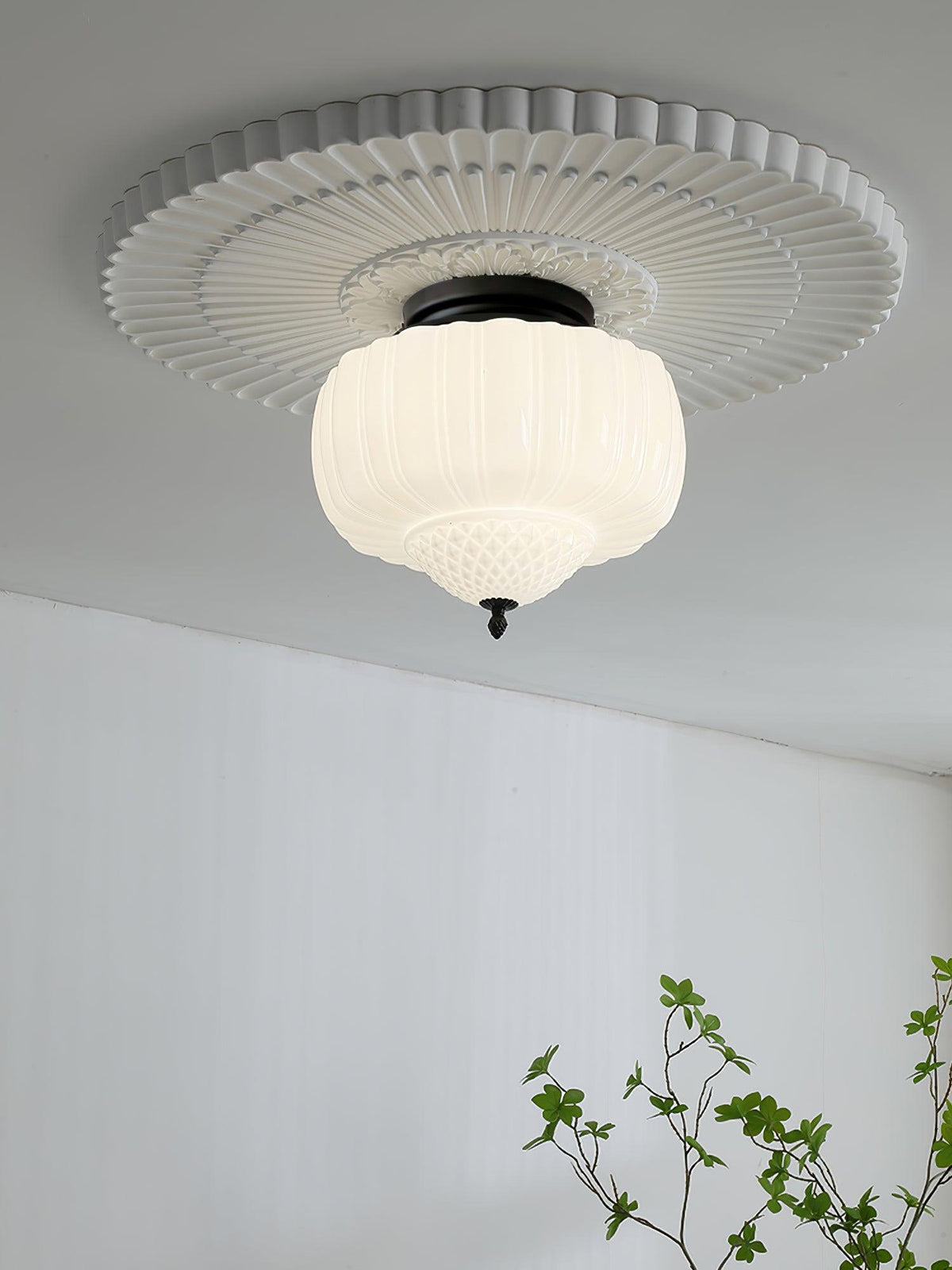 Clérachic ceiling light with a ribbed white glass shade and black canopy, set within a fluted plaster ceiling rose above a white wall.
